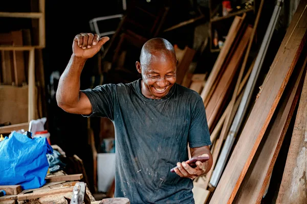 A small business owner smiling and celebrating while looking at his phone, representing the moment a qualified lead lands in the client's phone